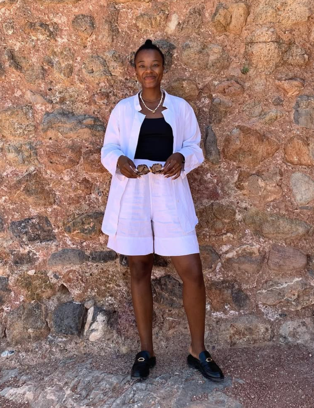 A bermuda feminina branca destaca-se como uma peça versátil e fresca para o verão. Combinada com uma blusa preta e um kimono leve, o look é ideal para ocasiões casuais. Os acessórios, como o colar e os óculos de sol, complementam a produção.