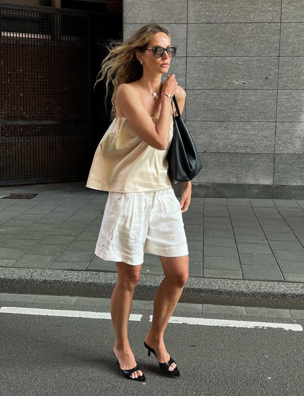 A bermuda feminina branca é a peça-chave do look, combinando conforto e estilo. Acompanhada de uma blusa de tecido leve e fluido, a produção ganha um toque sofisticado. O uso de sandálias de salto alto e uma bolsa preta completa a estética urbana.