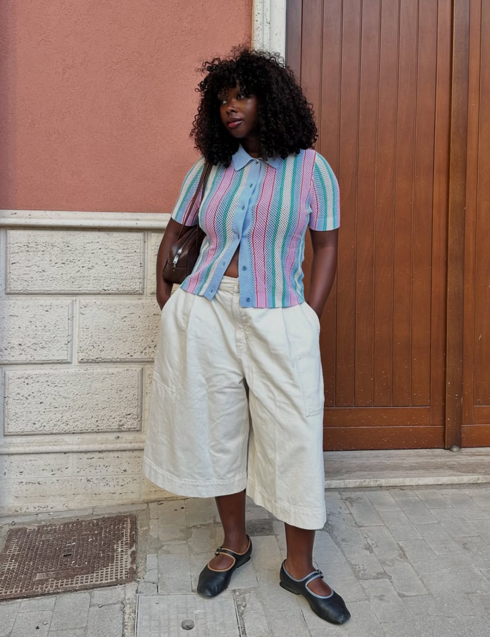 A bermuda feminina branca, com corte amplo e confortável, é destaque neste look moderno. Combinada com uma blusa de cores suaves e listras, ela traz um ar descontraído e estiloso. Os sapatos pretos complementam a produção, equilibrando o visual.