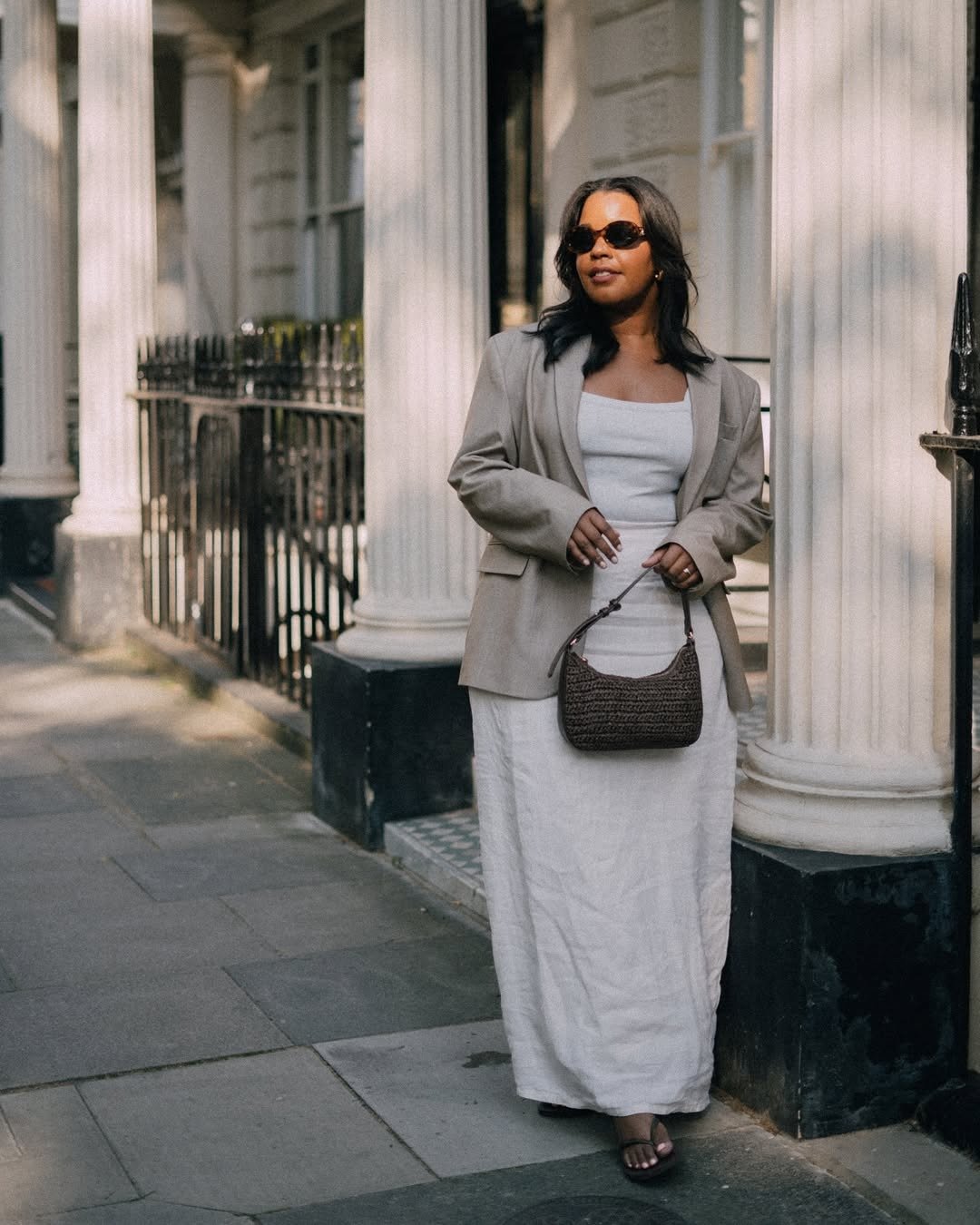 A imagem apresenta uma mulher elegante usando um vestido longo e justo, combinado com um blazer oversized em tom claro. Ela completa o look com chinelos, que trazem conforto e modernidade à produção. Como usar chinelo