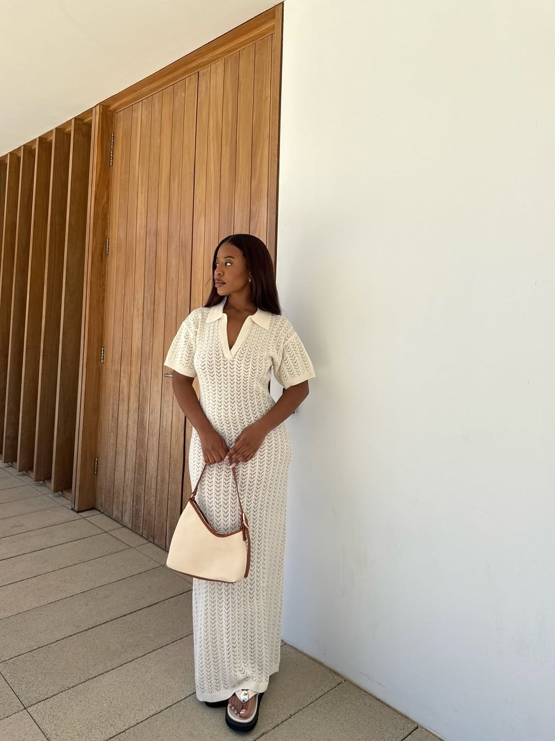 A imagem mostra uma mulher em um ambiente moderno, usando um vestido longo de crochê branco e chinelos elegantes, que combinam conforto e estilo. Como usar chinelo de forma estilosa