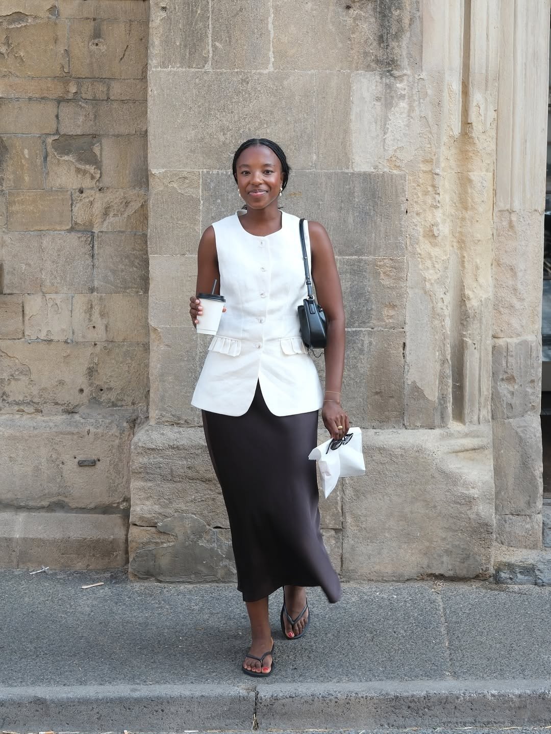 A imagem mostra uma mulher estilosa usando chinelos, combinando com uma blusa sem mangas branca e uma saia longa preta. Como usar chinelo