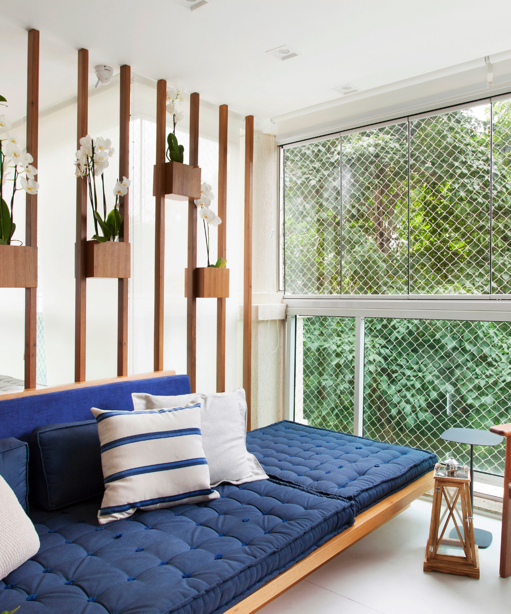 Sala com decoração em azul, sofás acolchoados, almofadas listradas e plantas em divisórias de madeira.