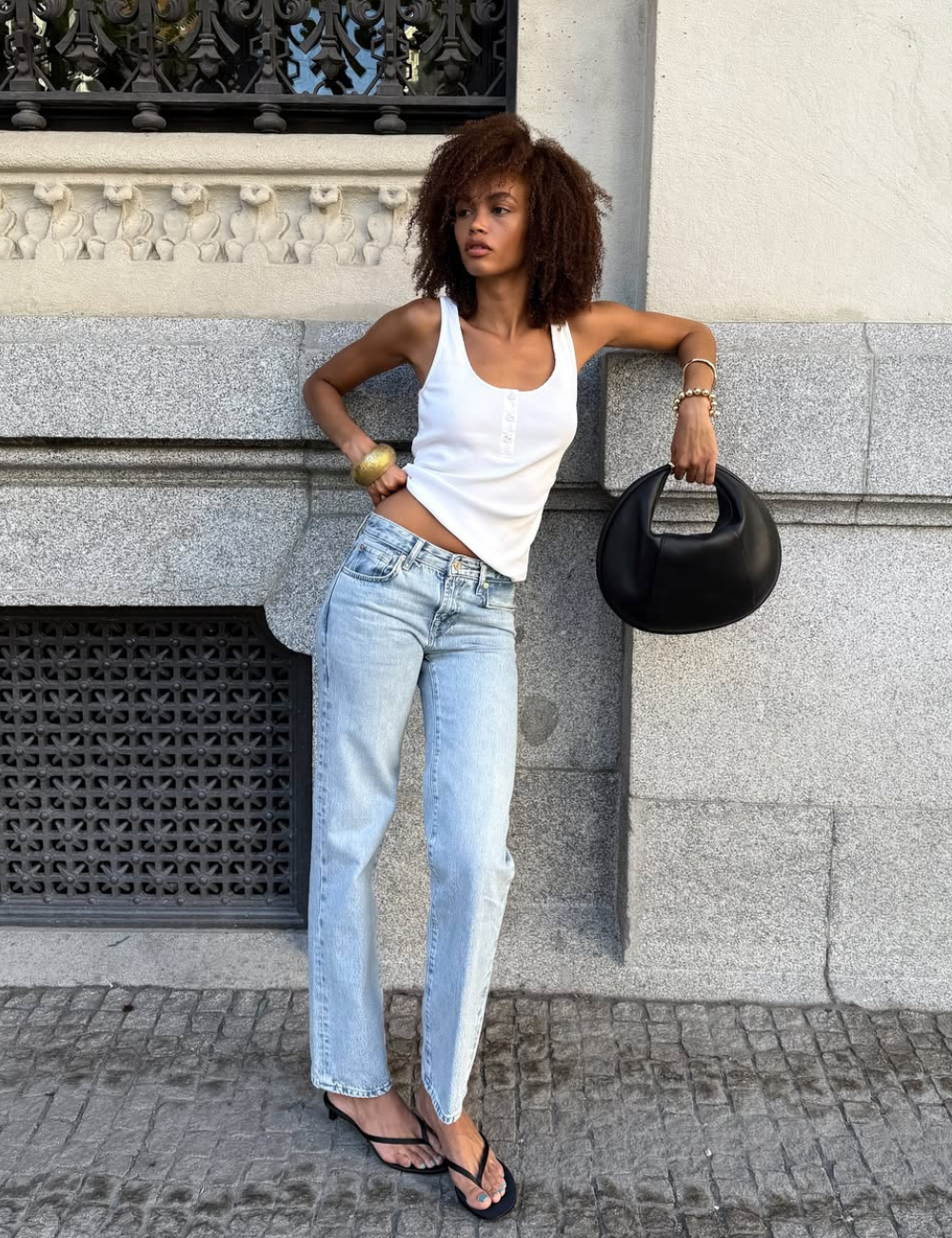 O tamanco é uma opção versátil e estilosa para compor looks casuais. Nesta imagem, a modelo combina tamancos pretos com uma camiseta branca e jeans claros, criando um visual moderno e descontraído.