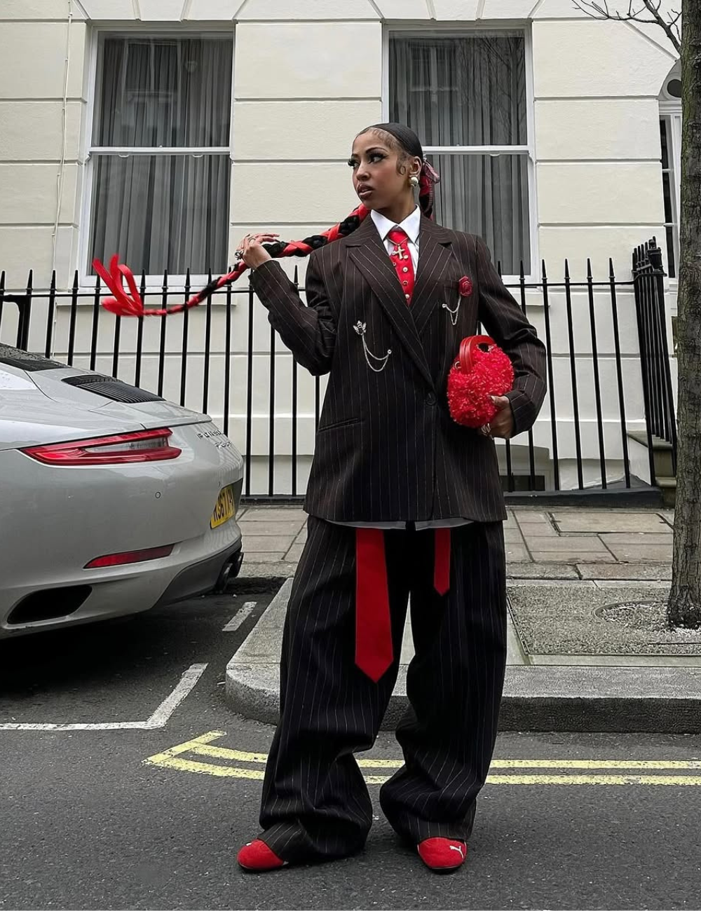 A imagem apresenta uma mulher estilosa usando um terno listrado em preto e branco com uma blusa branca e gravata vermelha, que complementa seus tênis vermelhos. O look é ousado, misturando elementos formais e casuais.