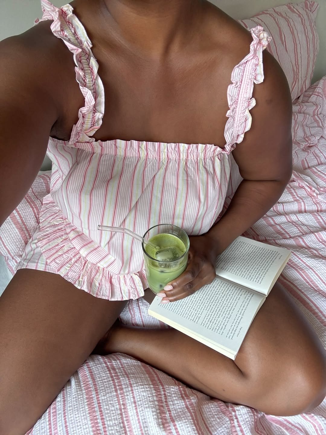 A imagem mostra uma pessoa sentada em uma cama com lençóis listrados em tons de rosa e branco. respondendo à pergunta: Qual é a cor do ano 2026?