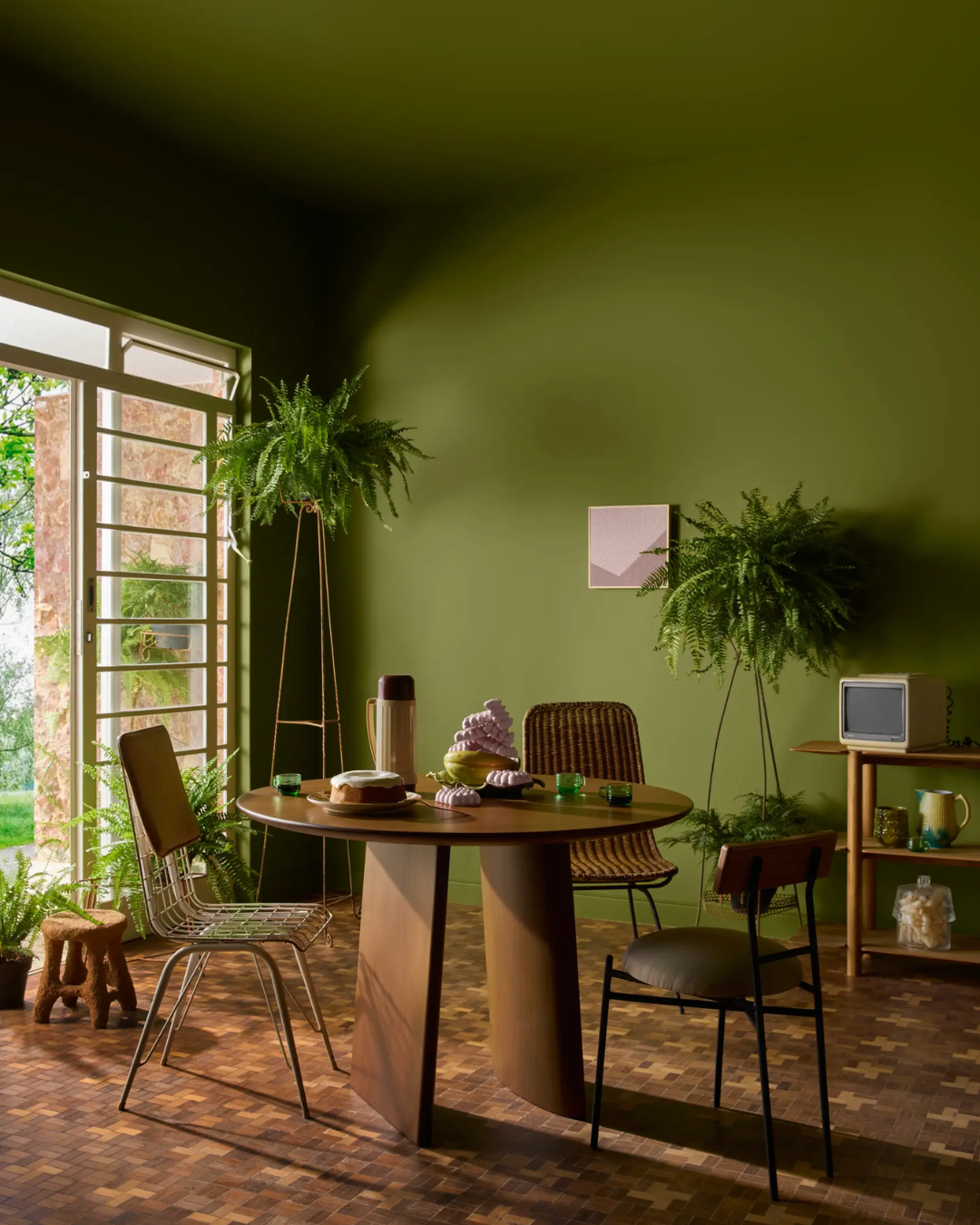 A imagem apresenta um ambiente acolhedor, com paredes na cor verde profundo, respondendo à pergunta: Qual é a cor do ano 2026?