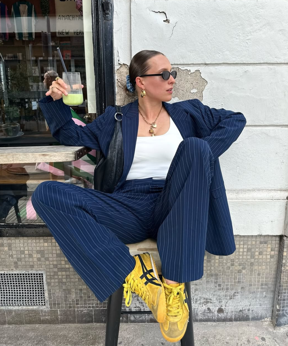 Pessoa usando conjunto de alfaiataria risca de giz azul escuro, camiseta branca e tênis amarelo vivo.