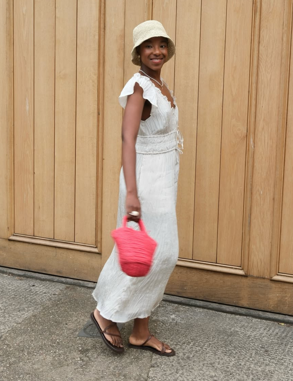 Uma mulher usa rasteirinhas confortáveis, ideais para o verão, combinadas com um vestido longo de tecido leve e fluido. O look é complementado por um chapéu de palha e uma bolsa pequena rosa, trazendo um toque de cor.