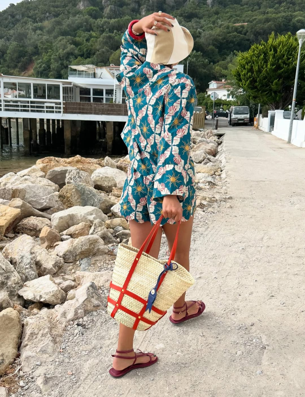 A composição destaca rasteirinhas para o verão, combinando estilo e conforto. A modelo usa uma roupa leve e estampada, ideal para dias quentes, e carrega uma bolsa de palha com detalhes coloridos, perfeita para a estação.