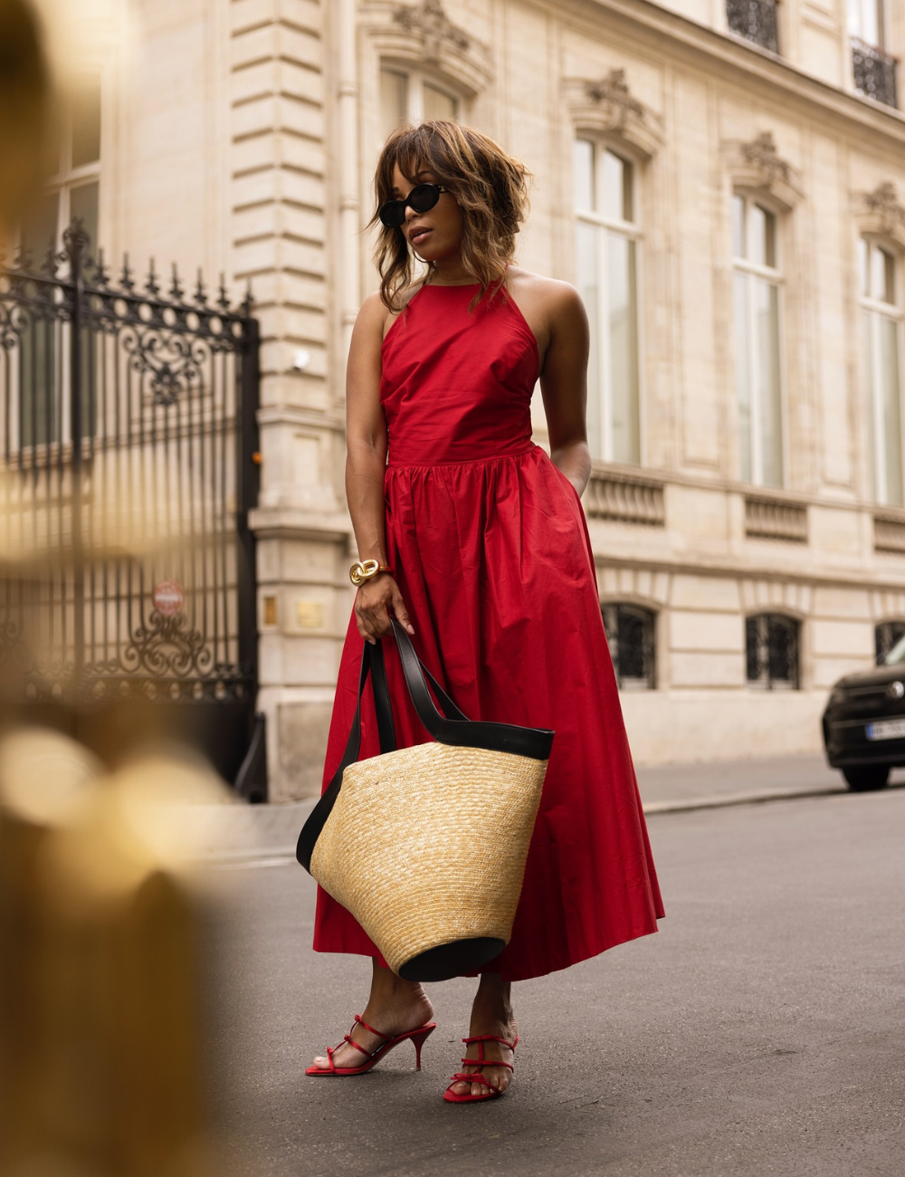 Vestido vermelho combinado com bolsa de palha e sandálias em uma rua urbana.