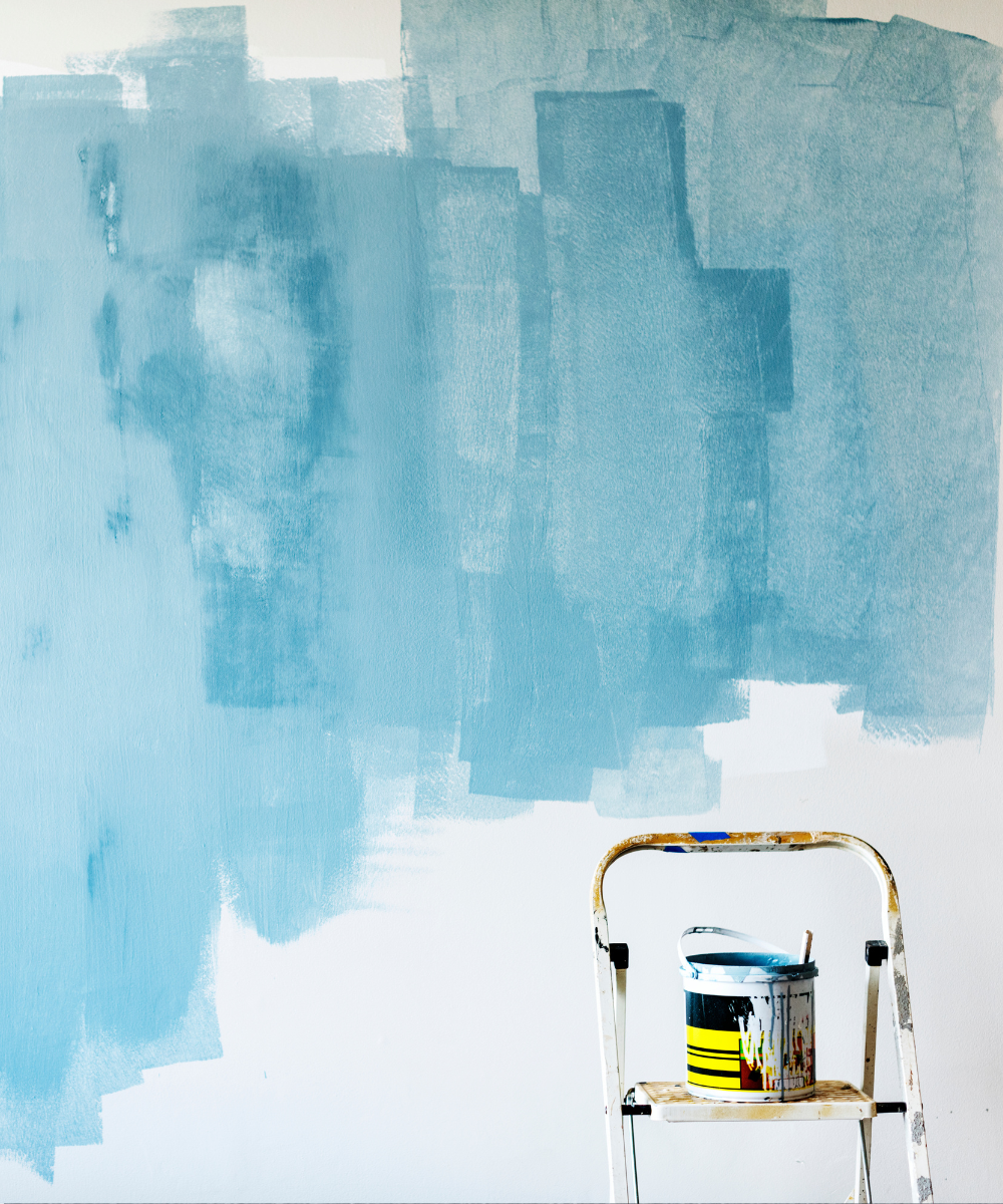 Paredes sendo pintadas de azul claro, com lata de tinta sobre escada; cores na decoração.