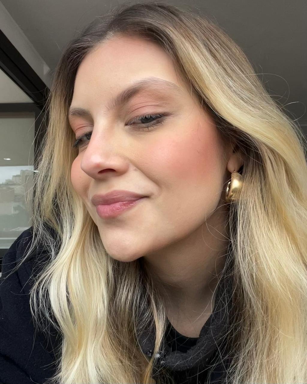 Mulher loira com maquiagem leve realça bochechas com blush em tom terracota.