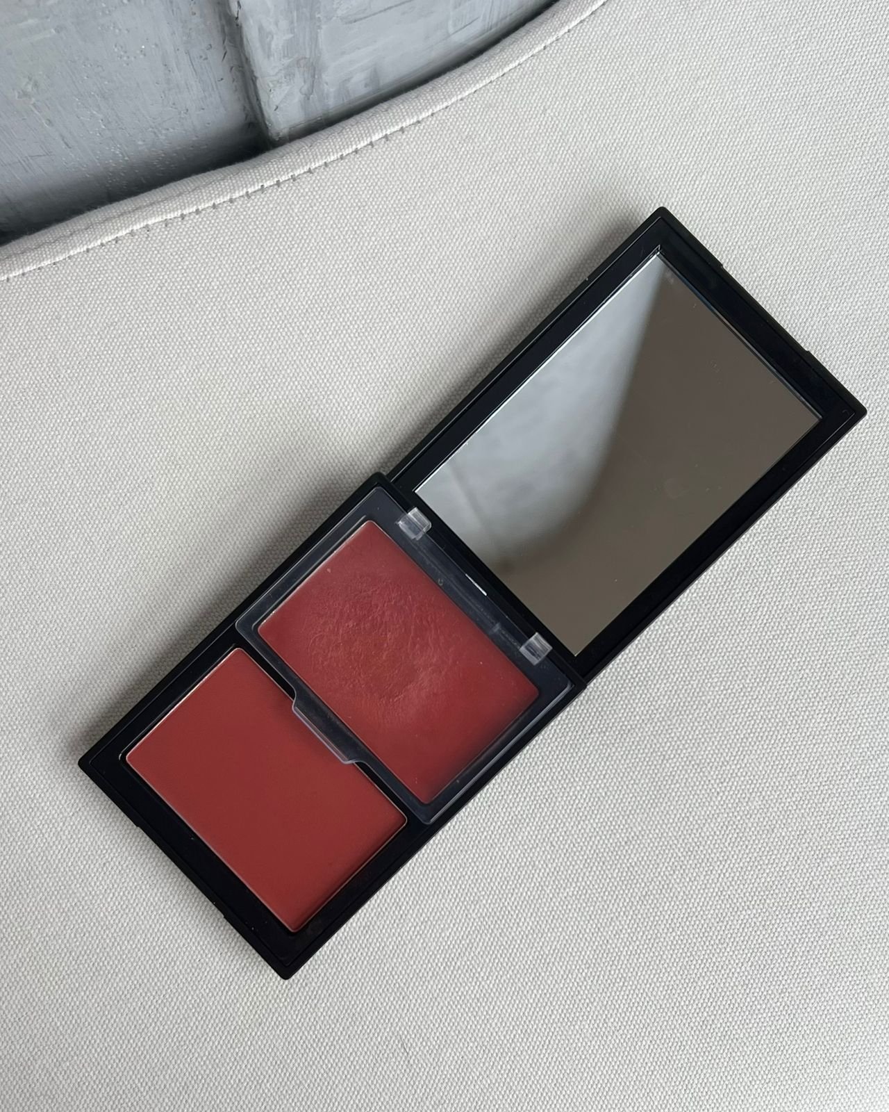 Estojo aberto com blush terracota e espelho na tampa, sobre superfície clara.