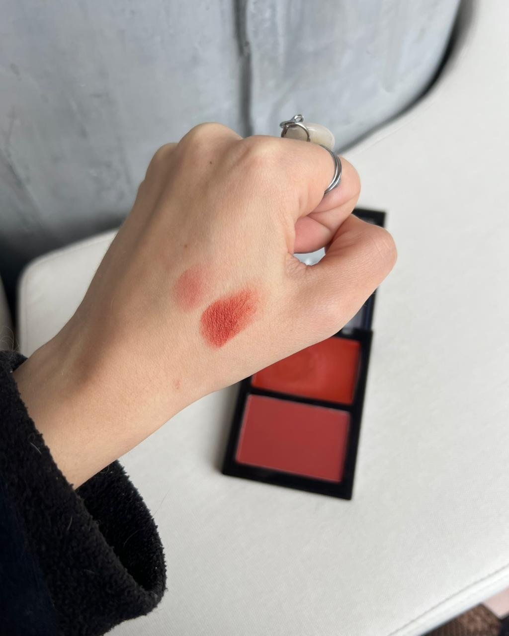 Blush terracota aplicado na mão de uma pessoa, próximo a uma paleta aberta com duas cores.