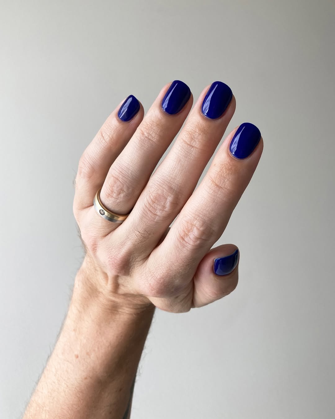 Mão com unhas pintadas de azul intenso, tendência para esmalte primavera verão 2026. Anel dourado no dedo anelar.