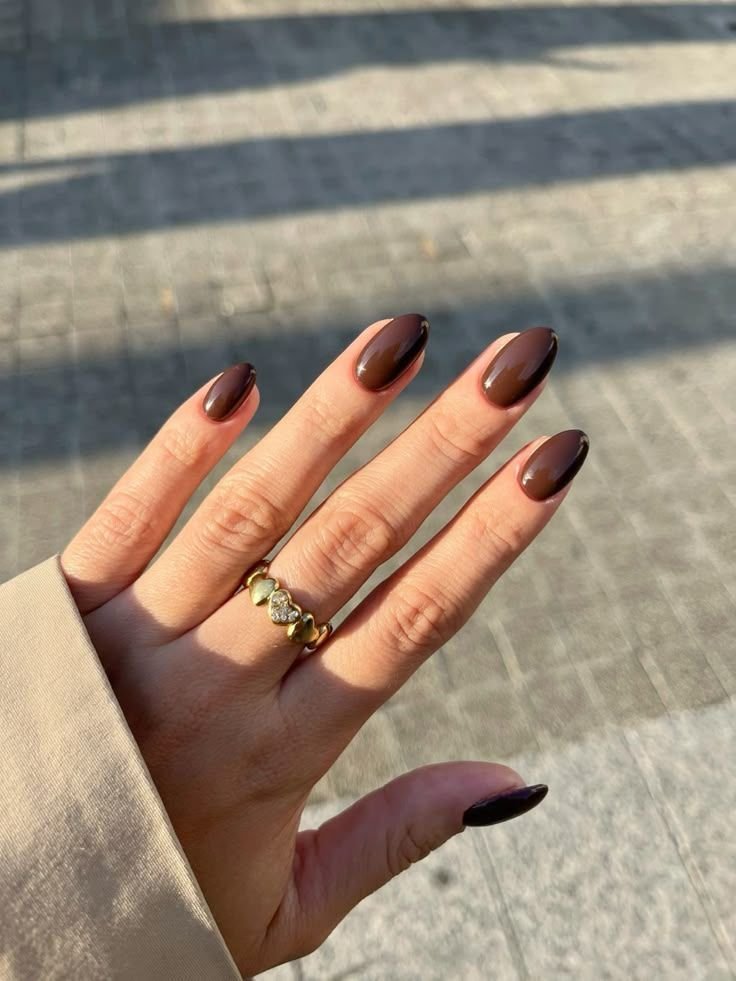 Unhas em tom marrom com esmalte primavera verão 2026 e anel dourado com pedras brilhantes.