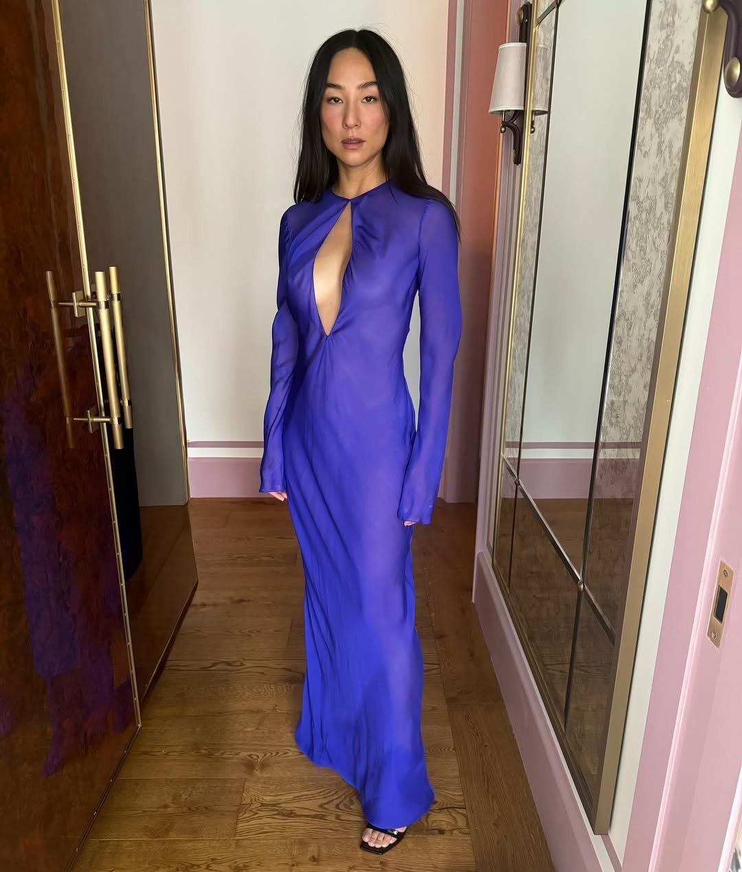 O estilo da Greta Lee é marcado por um vestido longo e justo, na cor roxa vibrante, que destaca sua silhueta. A peça possui um decote profundo com um recorte inovador, conferindo um toque de ousadia e sofisticação. Com mangas longas e tecido leve, o look