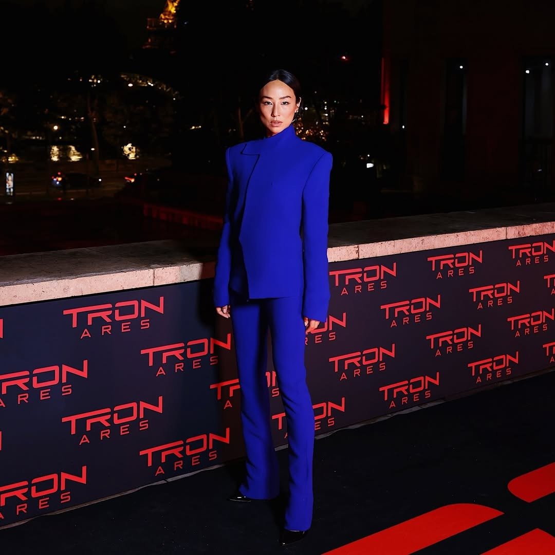 Greta Lee exibe um impressionante visual em um elegante conjunto azul, que destaca a silhueta moderna e sofisticada. O blazer, com cortes estruturados e mangas longas, é combinado com calças ajustadas, criando uma estética poderosa e contemporânea. O cená
