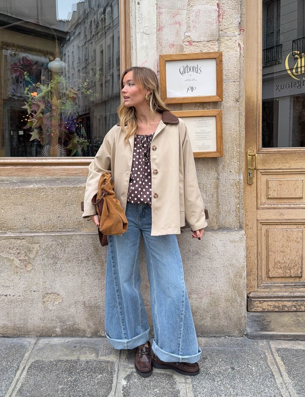Mulher de pé em uma rua parisiense olhando para baixo enquanto mexe nos cabelos.