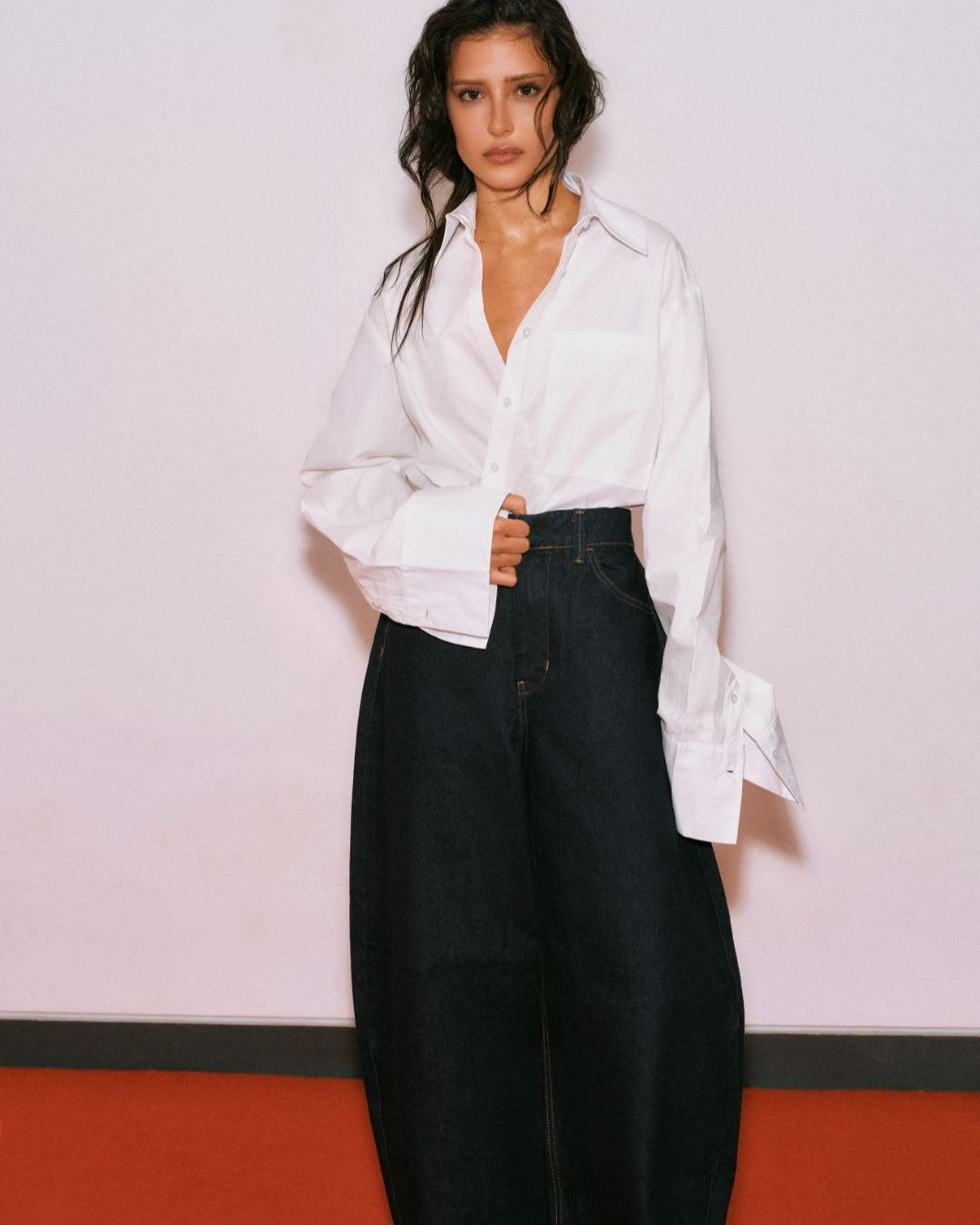 A coleção Renner + Livia traz um look contemporâneo, destacando uma camisa branca oversized e uma calça jeans ampla. A combinação transmite um estilo casual e elegante, ideal para diversas ocasiões. O cabelo solto e levemente ondulado complementa o visual