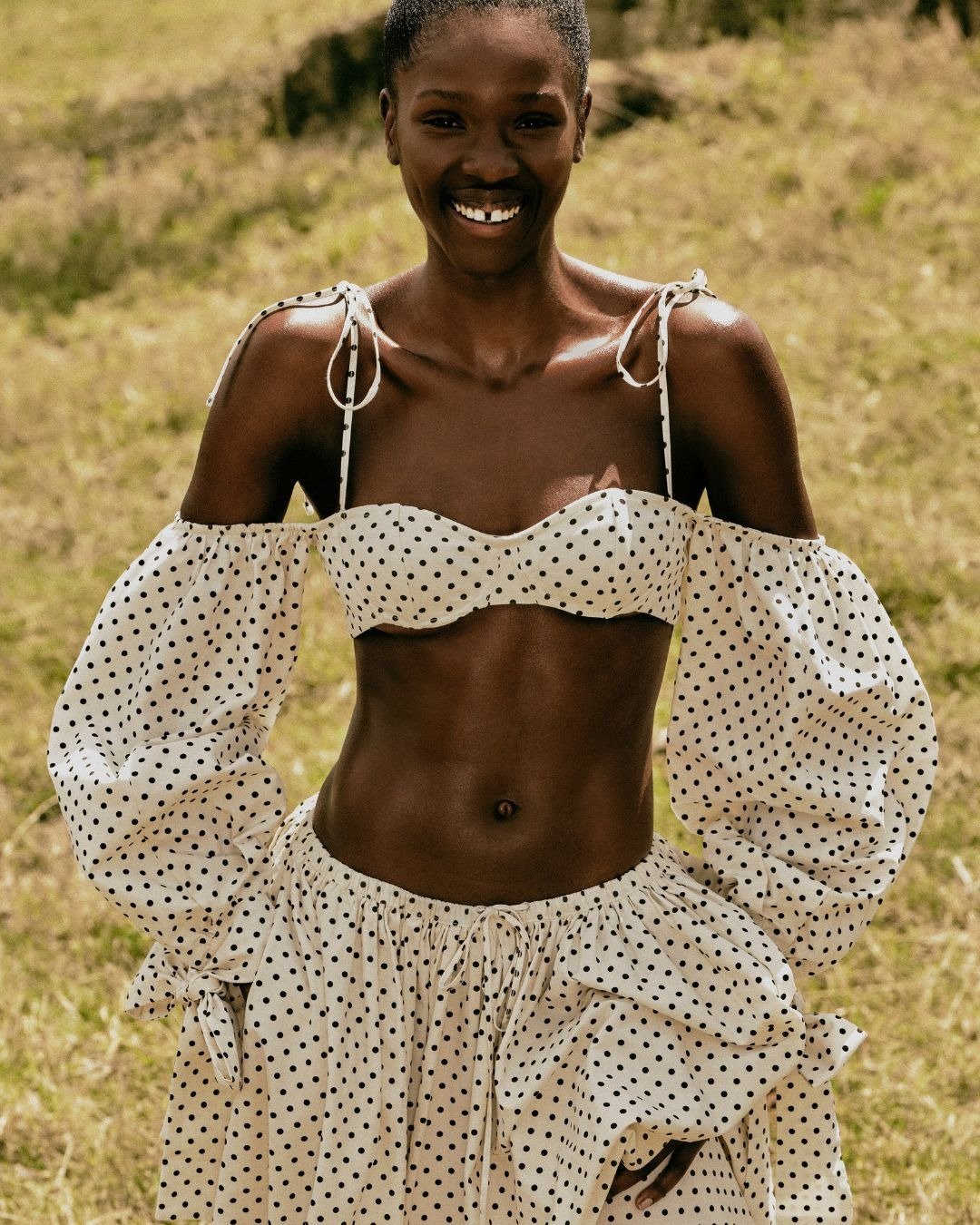 A coleção Renner + Livia apresenta um conjunto estiloso com blusa cropped de poás e mangas bufantes, combinada com uma saia fluida. O look destaca a silhueta e traz um ar descontraído e elegante, ideal para dias ensolarados. A paleta de cores neutras e o