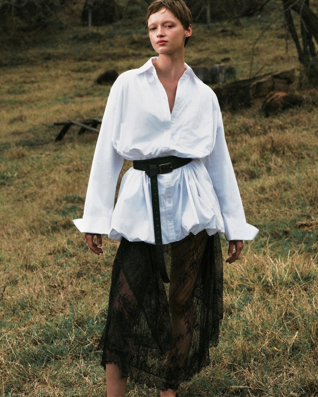 A coleção Renner + Livia traz uma proposta ousada e contemporânea, destacando uma blusa branca oversized, que combina conforto e sofisticação. O cinto preto marca a cintura, enquanto a saia preta de renda adiciona um toque de elegância e transparência. O