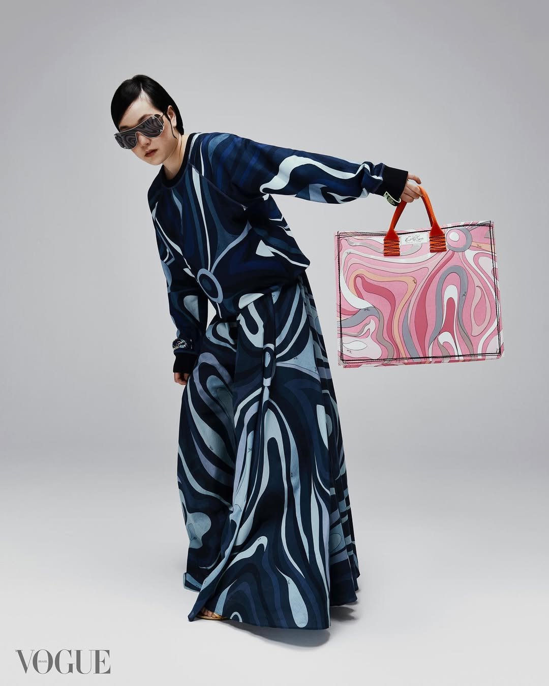 Mulher com conjunto com estampa psicodélica azul e bolsa rosa vibrante, em referência à moda dos anos 60.