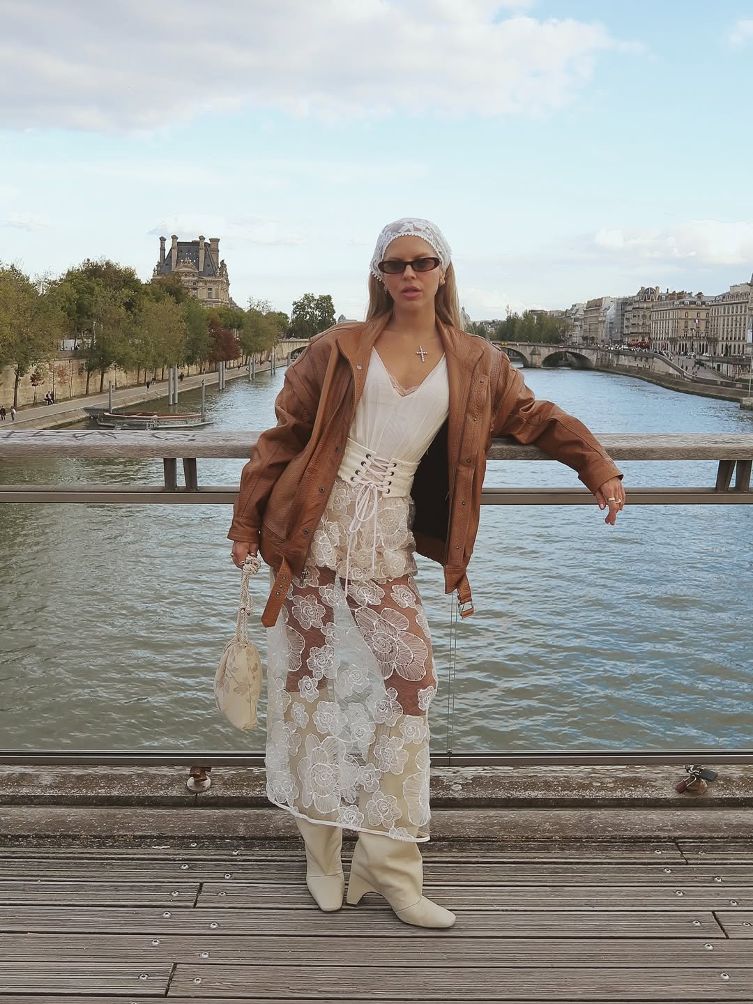 Mulher com lenço no cabelo, vestido rendado, jaqueta marrom e botas, em look inspirado na moda anos 60.