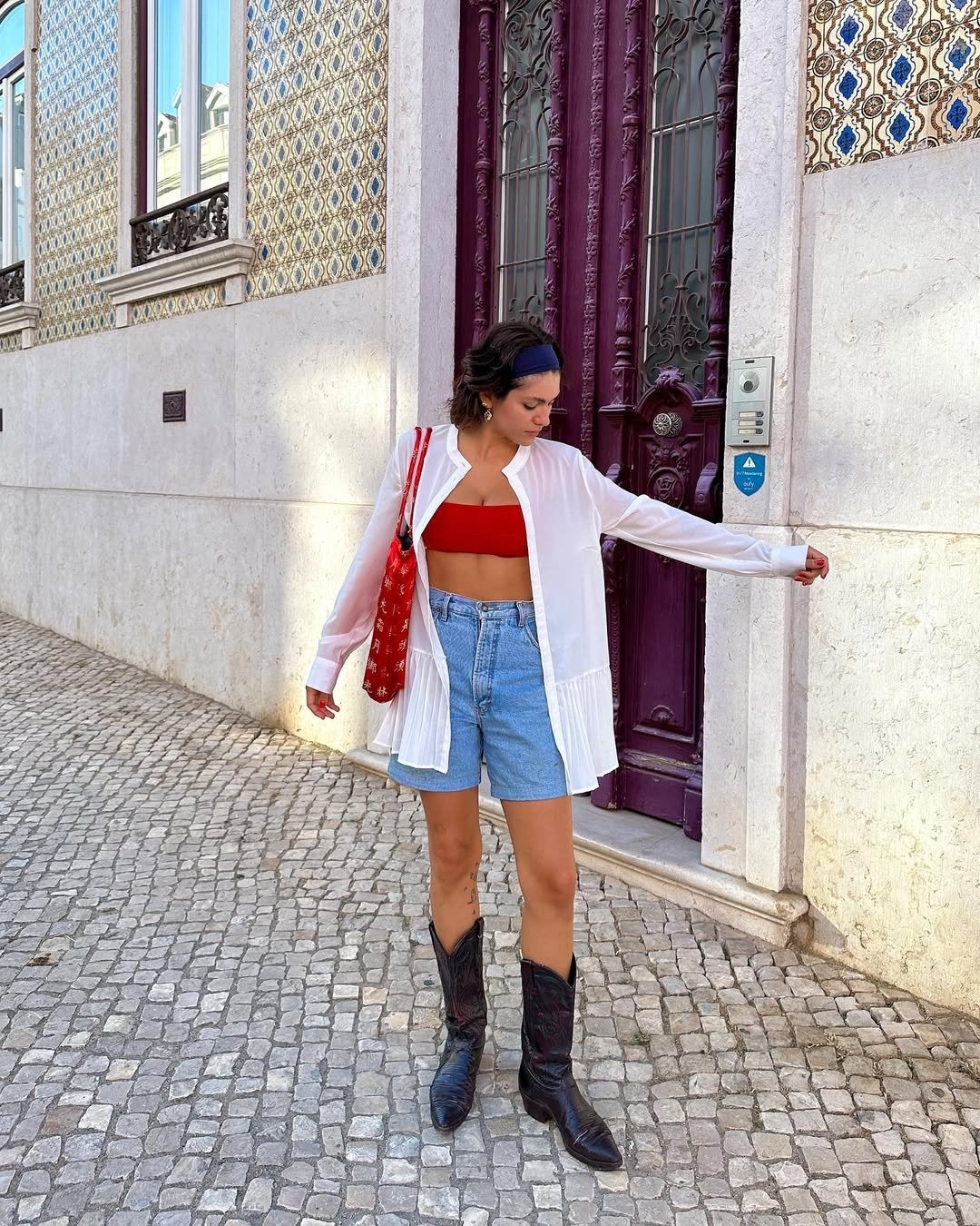 Mulher usando look com bermuda jeans, combinando uma blusa branca leve e cropped vermelho.