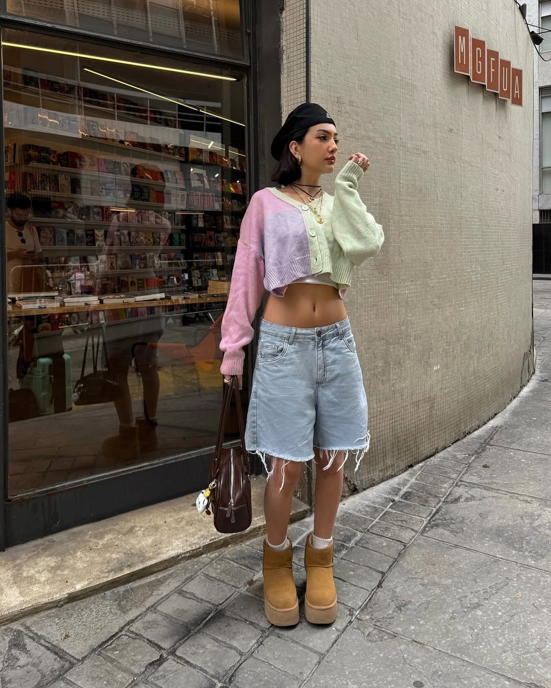 Mulher usando look com bermuda jeans, cropped manga longa e ugg boots. O cropped em tons de rosa e verde destaca a silhueta.