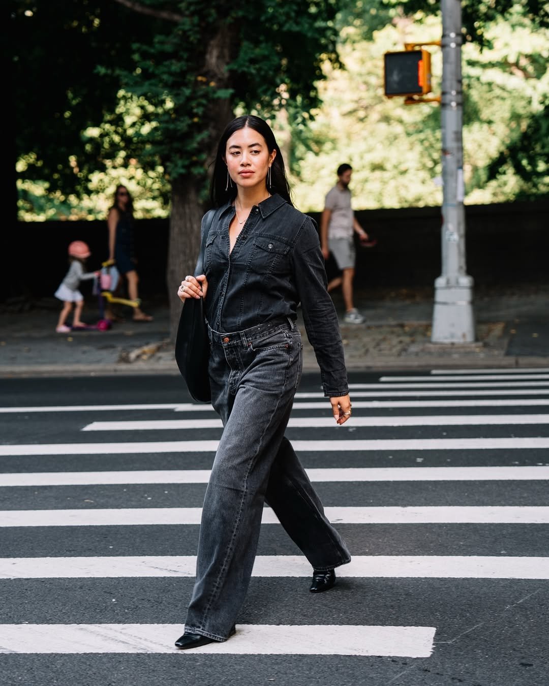 Mulher atravessa faixa de pedestres usando look com calça preta jeans de cintura alta e camisa preta combinando.