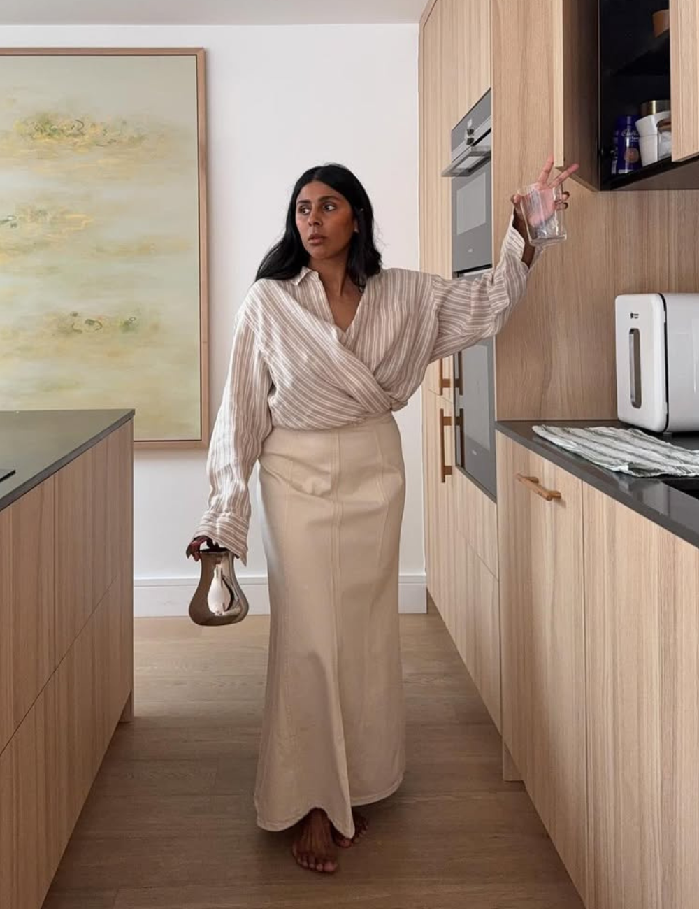 O look com camisa listrada feminina apresenta uma blusa de mangas longas em tons neutros, com listras que adicionam um toque de elegância. A combinação com uma saia longa de cor clara cria um visual sofisticado e moderno.