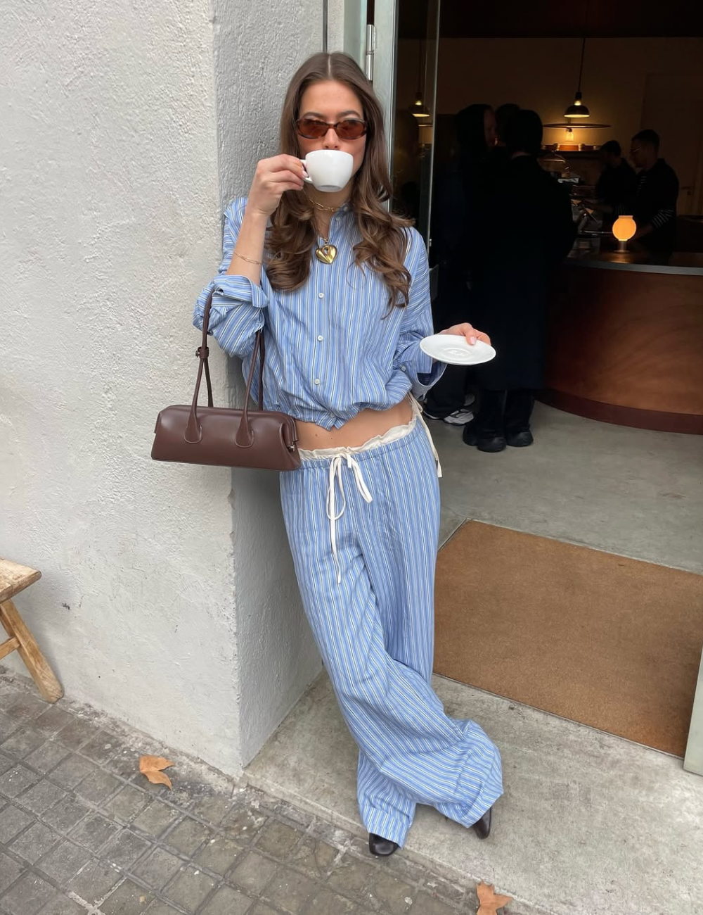 O look com camisa listrada feminina apresenta uma combinação estilosa e descontraída. A camisa azul com listras brancas é usada de forma cropped, destacando a cintura. A calça larga complementa o visual.