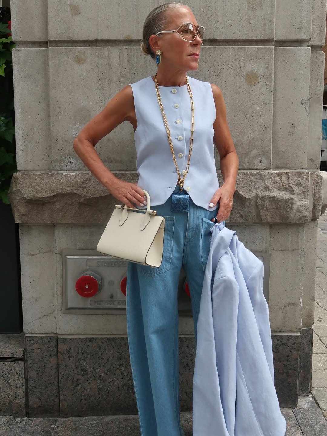 look com colete azul claro, óculos grandes e bolsa bege.
