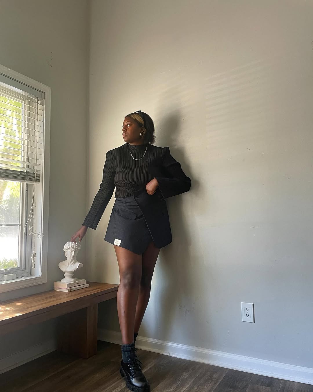 Mulher com look com mocassim tratorado, blusa de manga longa preta com texturas, saia preta e blazer oversized, complementando com acessórios delicados e uma postura elegante.