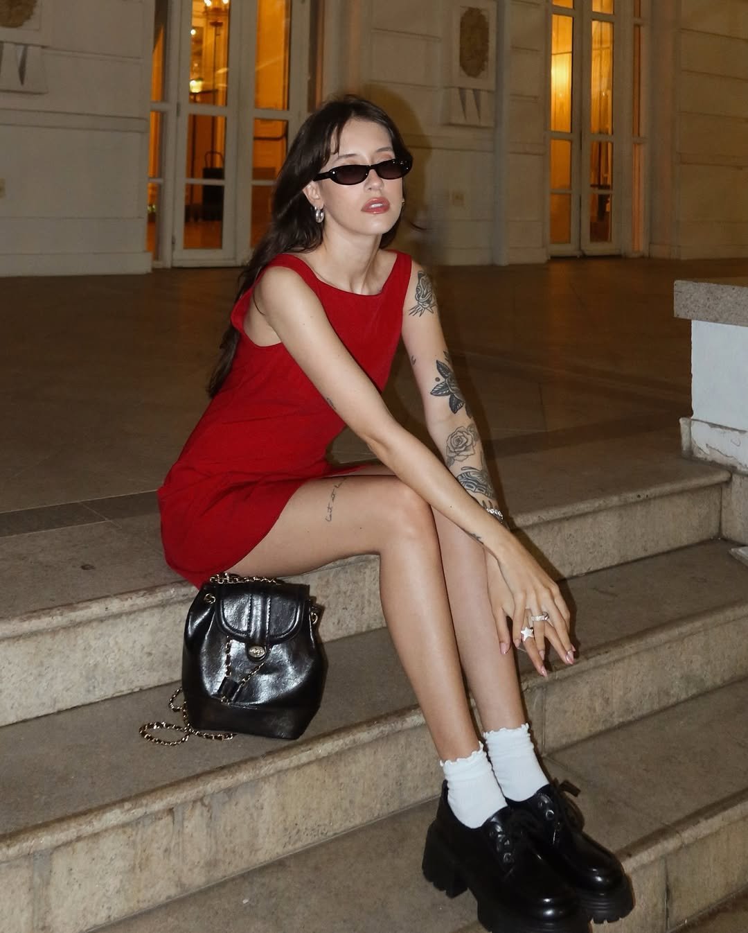 Mulher com look com mocassim tratorado, vestido vermelho justo, óculos escuros, meias brancas e bolsa preta.