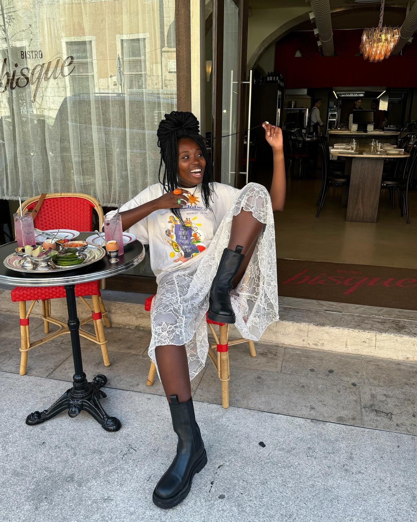 O look meia-estação é destacado por uma combinação de peças que equilibram conforto e estilo. A modelo usa uma camiseta oversized com estampa vibrante, complementada por uma saia longa de renda branca, que traz leveza ao visual.