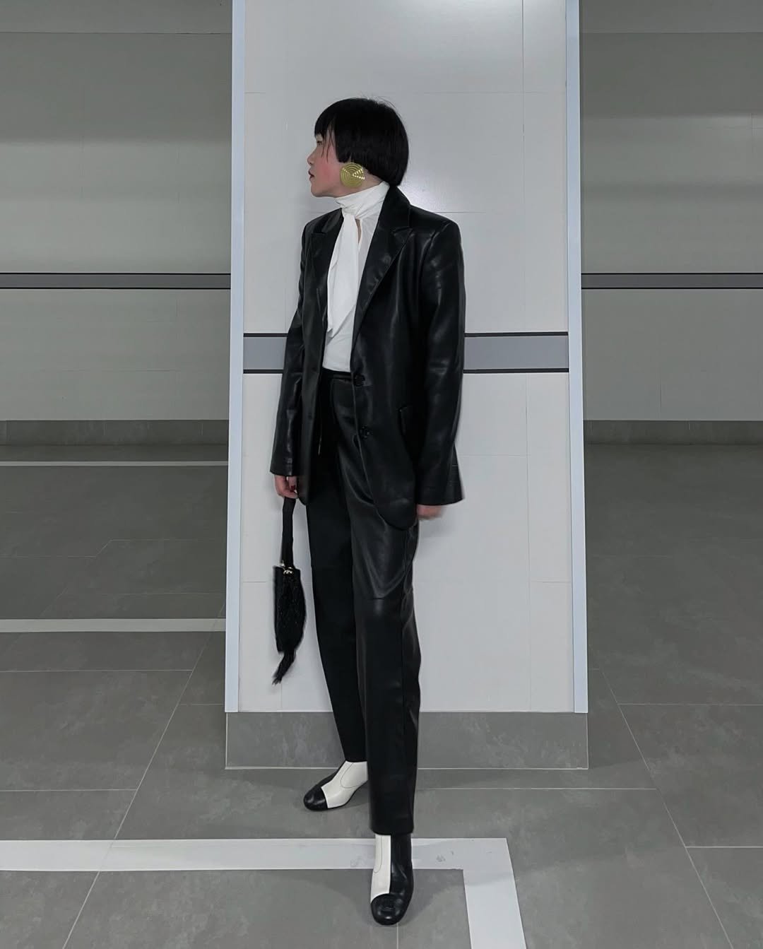 Mulher com estilo elegante e moderno usa look com calça de couro preta, blazer de couro, blusa branca de gola alta e botinhas bicolores.