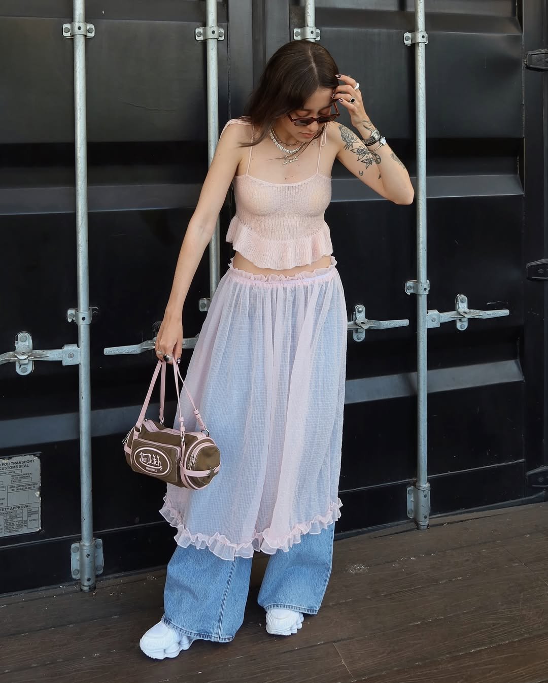 Mulher dando opção de looks com rosa bebê usando conjunto com jeans largo e segurando bolsa.