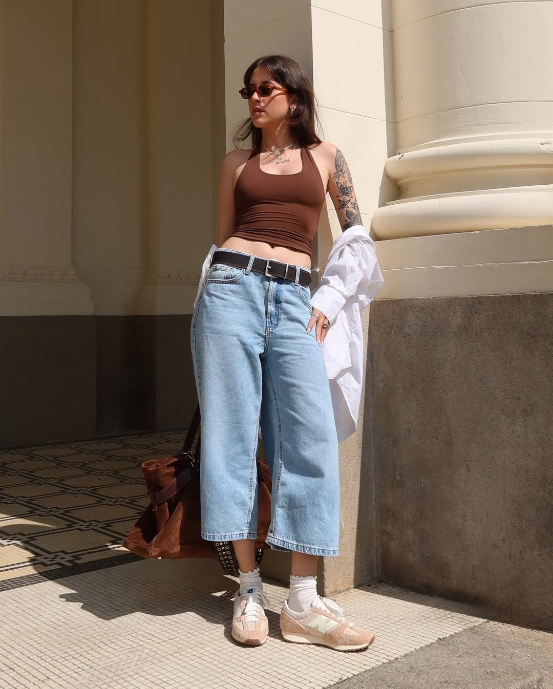 Mulher com calça pantacourt jeans e top cropped marrom, ótimo look para barzinho à noite com tênis.