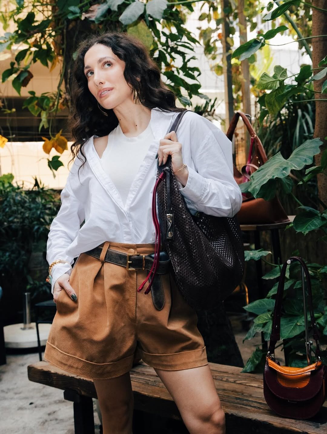 Mulher com look para barzinho à noite, usando camisa branca oversized, regata e shorts de couro caramelo.