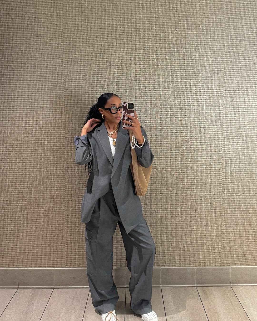 Pessoa usando terno cinza e look com tênis branco, fotografando em espelho. O look é casual e elegante, complementado por acessórios.