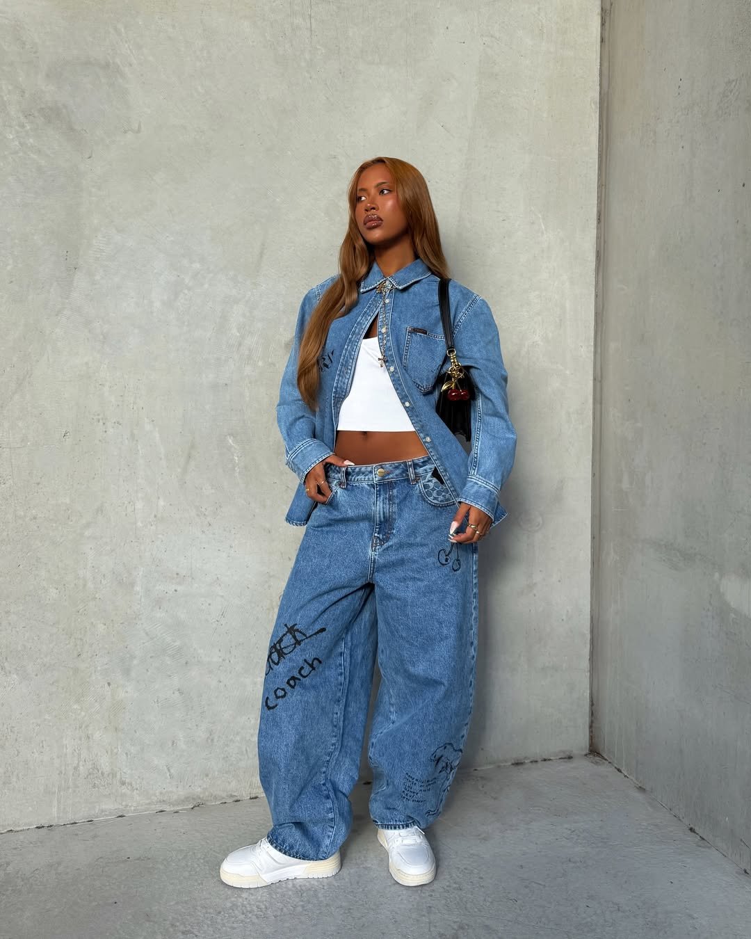 Pessoa com look casual, usando jaqueta jeans, top branco, calça ampla jeans e look com tênis branco.