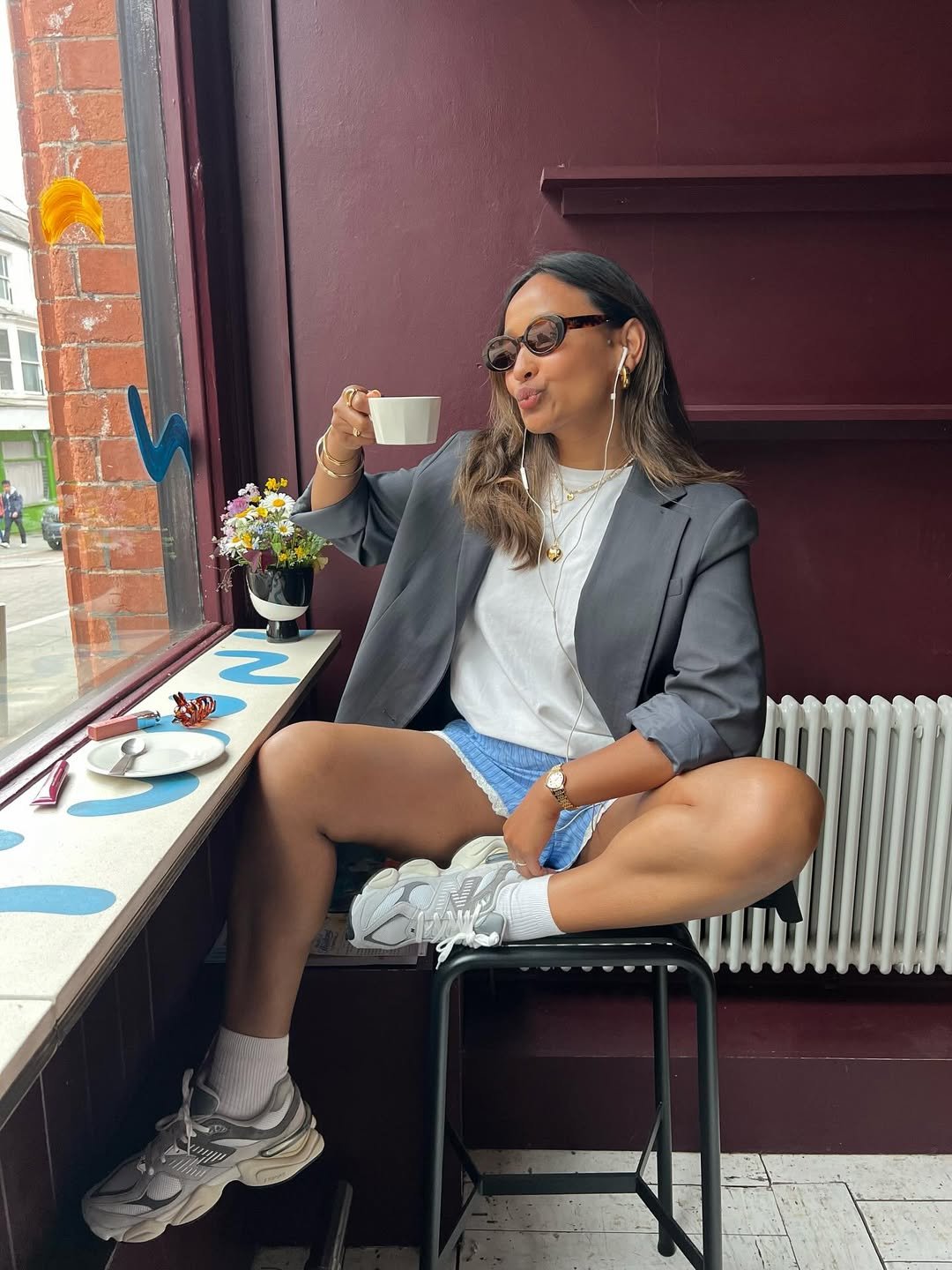 Mulher em vestido azul claro com look com tênis branco, parada na calçada em frente a uma loja.