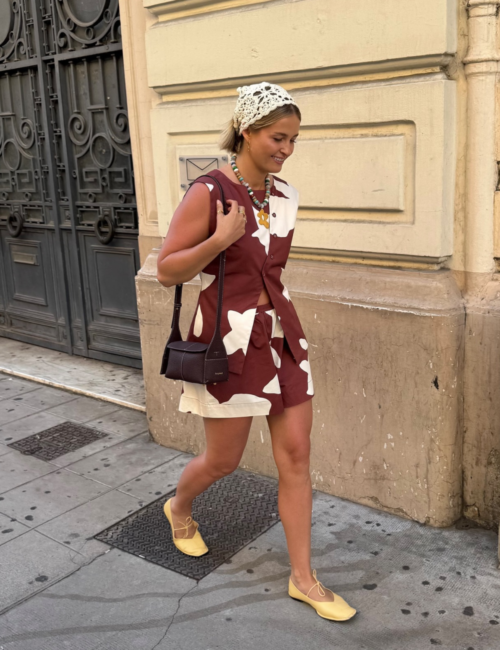 Pessoa usando vestido estampado marrom e branco, bolsa preta e touca de crochê branca, caminhando em ambiente urbano.