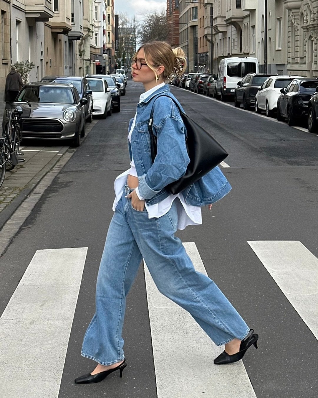 Pessoa atravessa rua vestindo jaqueta e calça jeans com blusa branca e salto preto.