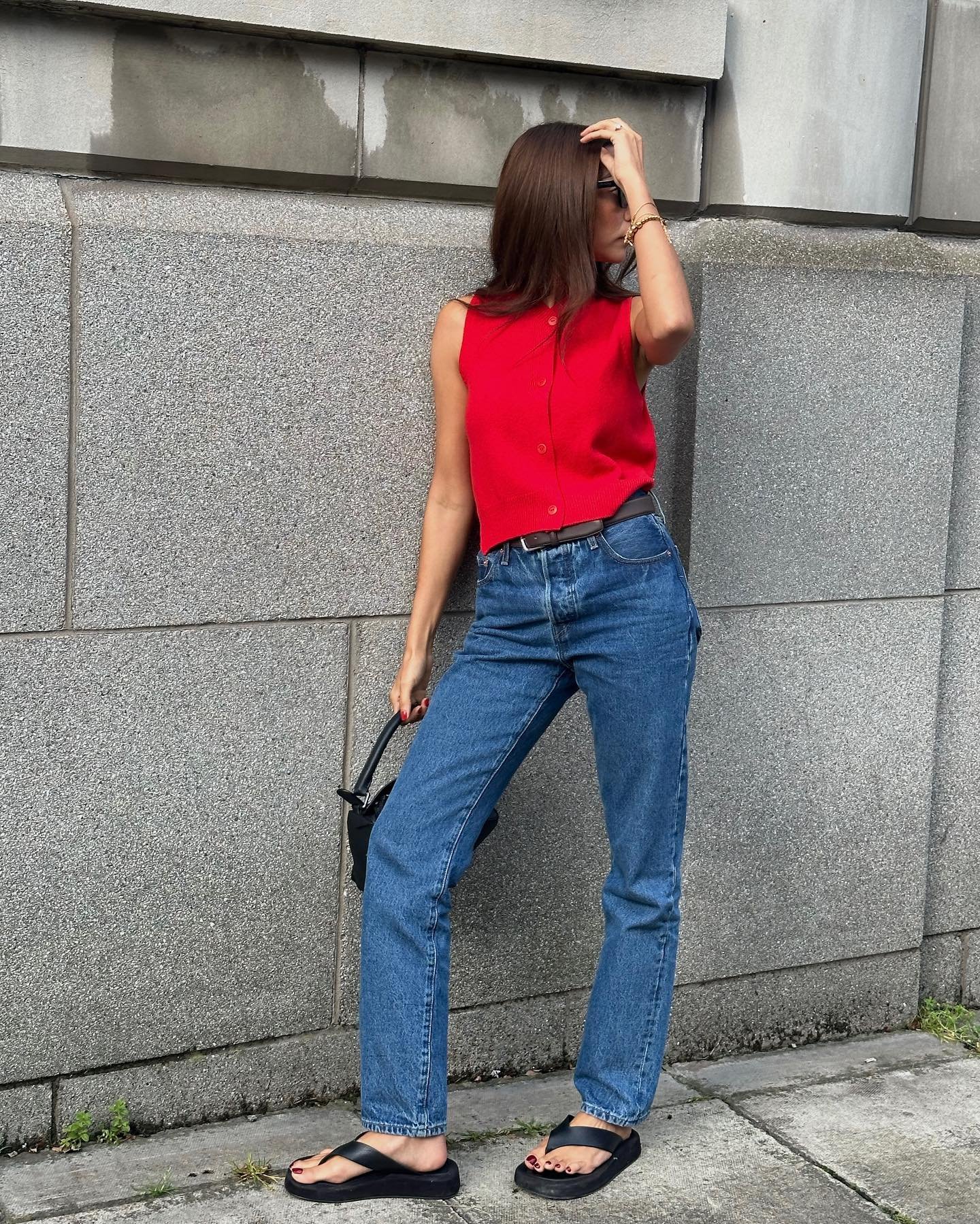 Pessoa com colete vermelho e calça jeans, segurando bolsa preta.