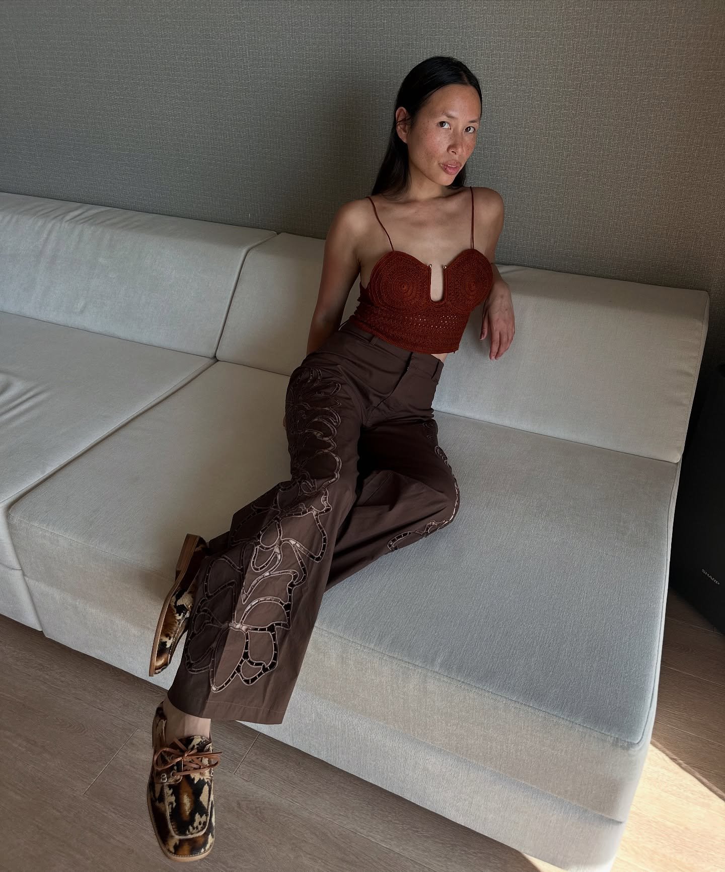 Mulher sentada em um sofá, usando calça marrom feminina com detalhes em renda e sapatos estampados.
