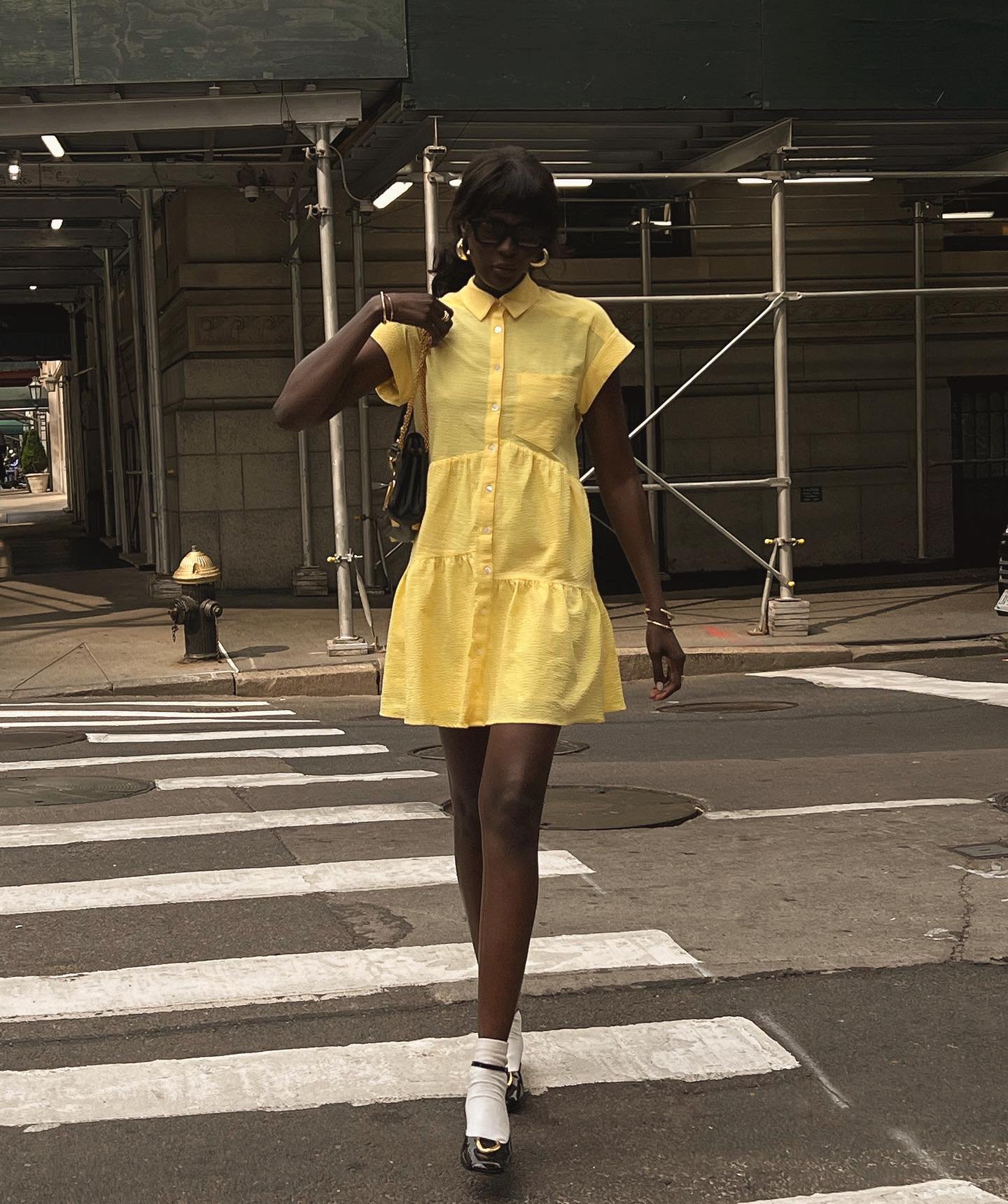 Pessoa usando chemise amarela em um cruzamento urbano, carregando bolsa preta.